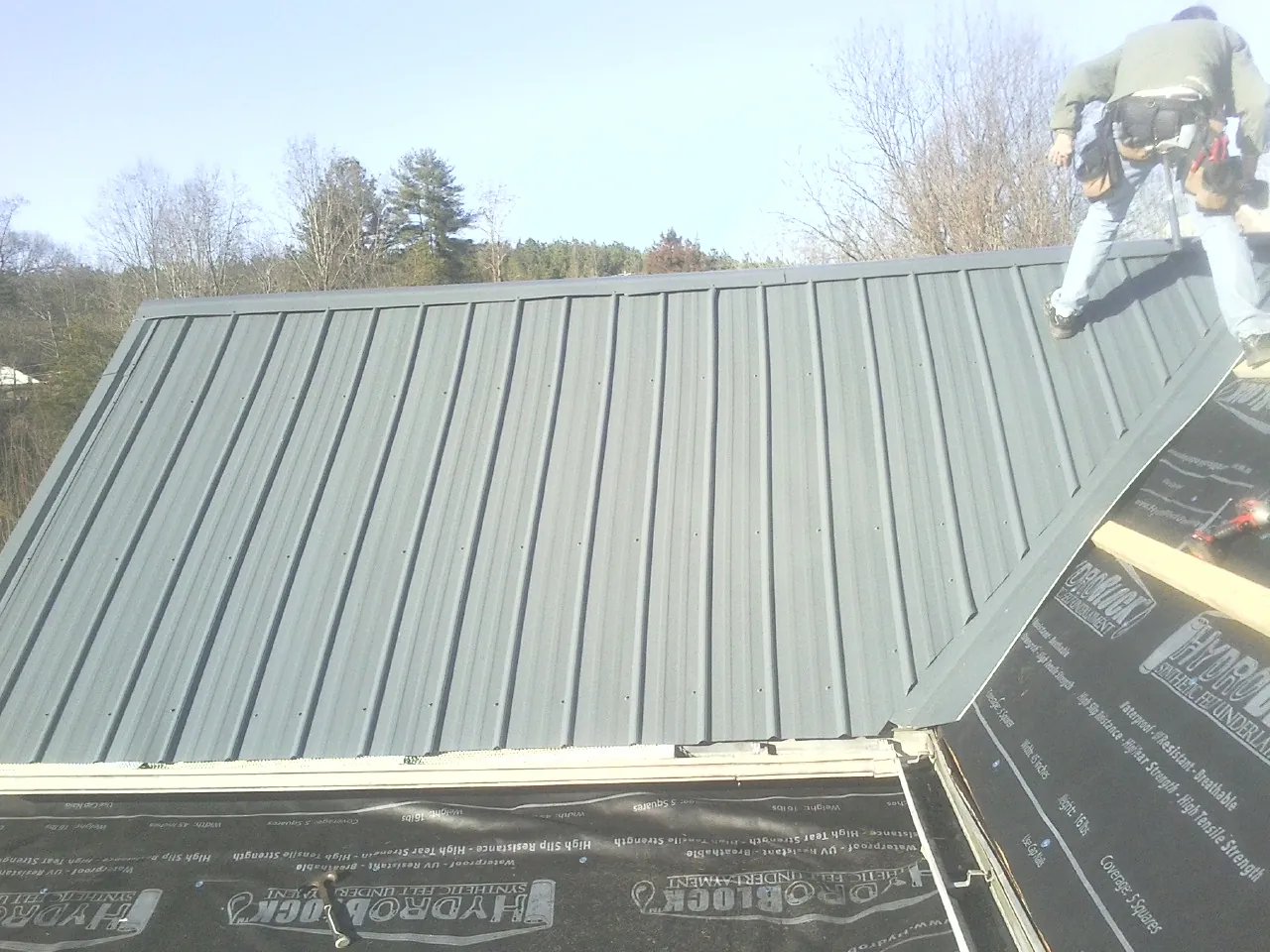 Crew installing dark green standing seam panels over synthetic underlayment in Madisonville