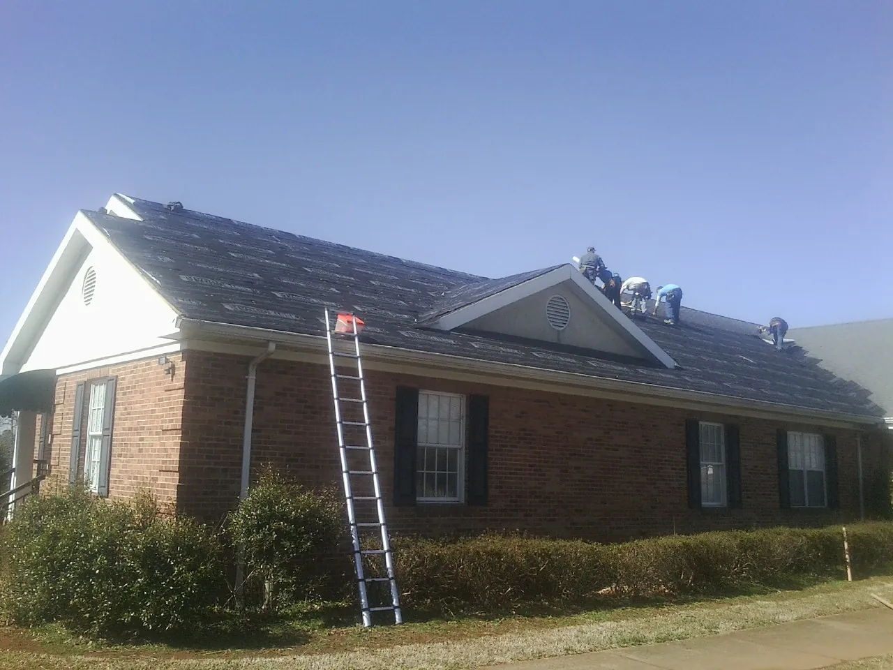 Crew tearing shingles off a brick ranch roof with a ladder set — Metal Roof Repair work by our crew in Madisonville