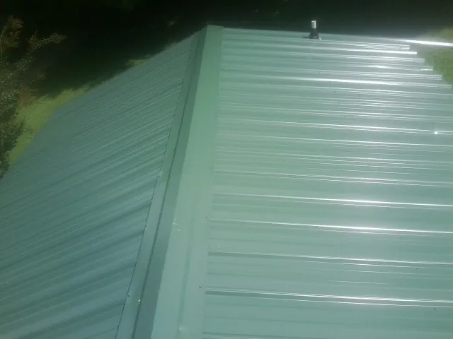 New green metal panels meeting at the ridge of a roof — Flat Roof Repair work by our crew in Madisonville