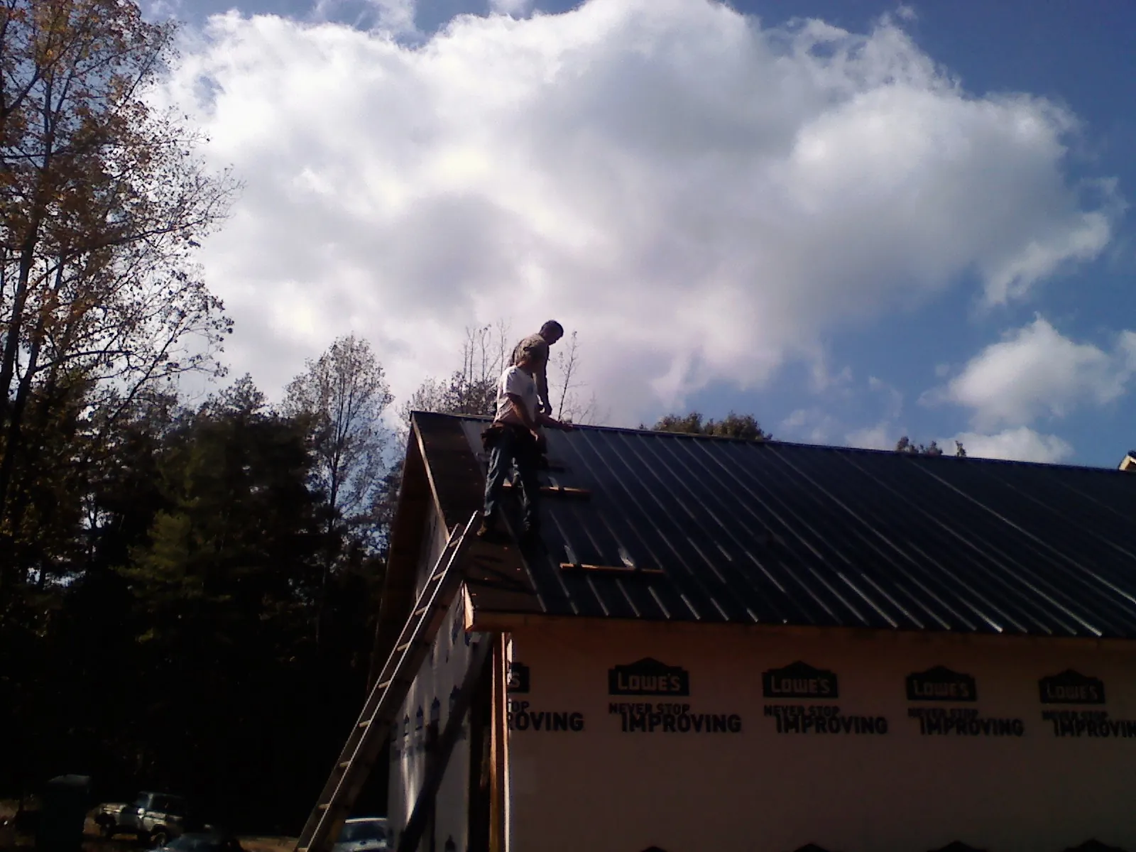 Roofer fastening dark metal panels high against a cloudy sky, from a Roof Inspection job in Madisonville